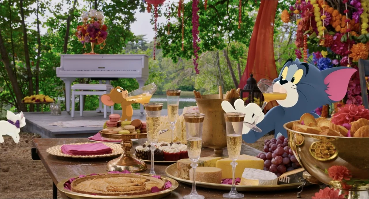 Tom & Jerry (2021) movie still: medium — An outdoor banquet table is filled with fruits, pastries, and drinks under trees. Tom the cat and Jerry the…