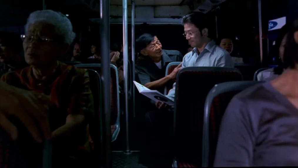 Last Life in the Universe (2003) movie still: medium — Interior of a city bus at night with passengers seated in dim light. An older man leans…