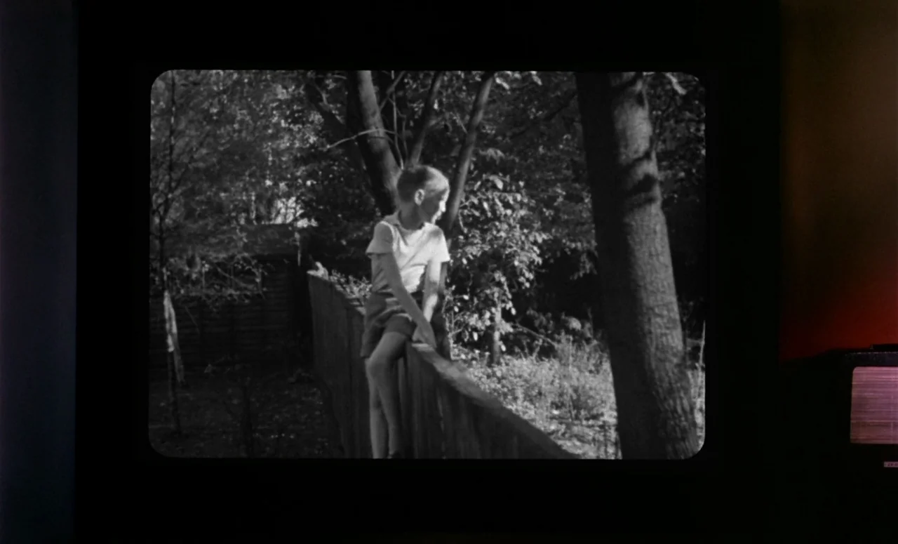 Peeping Tom (1960) movie still: medium — A young boy sits on top of a wooden backyard fence surrounded by trees. The boy gazes toward the right side…