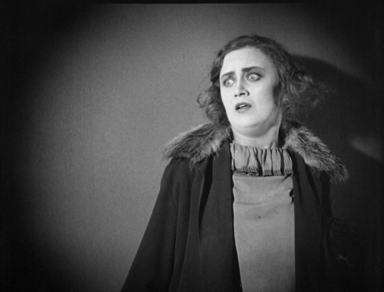 The Hands of Orlac (1924) movie still: medium — A plain interior background with a solid wall surface creates a simple portrait frame. A woman with…