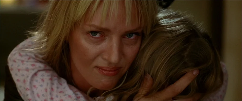 Kill Bill Vol. 2 (2004) movie still: closeup — A woman with blonde hair holds a child in a plain interior setting. The woman looks directly into the…