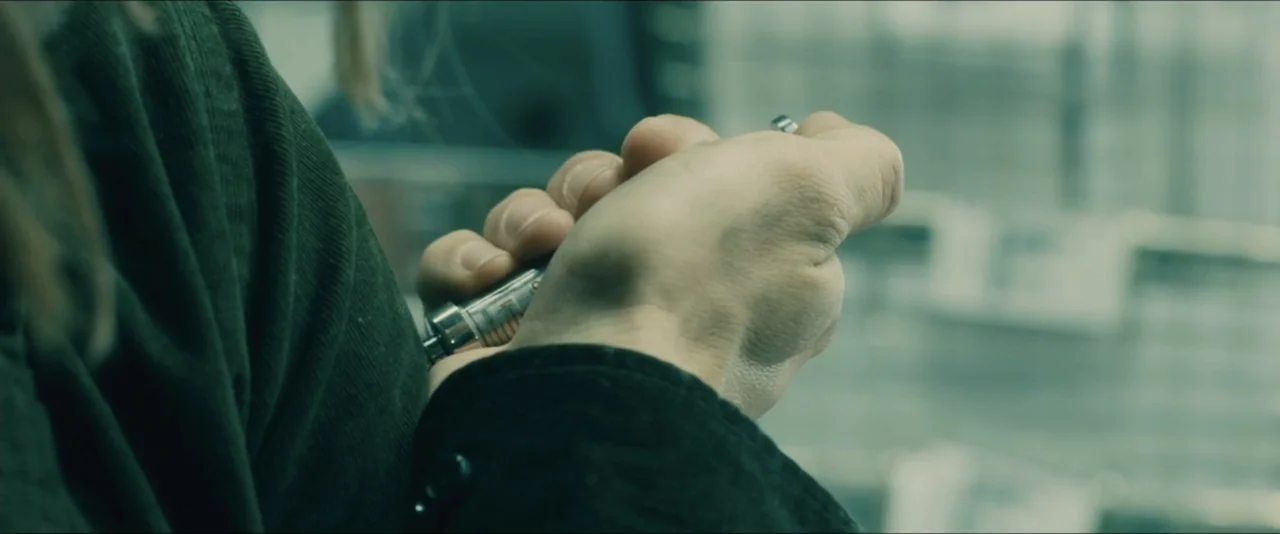 World War Z (2013) movie still: closeup — A close view of a hand holding a small, metallic, syringe-like cylinder. The background shows blurred…