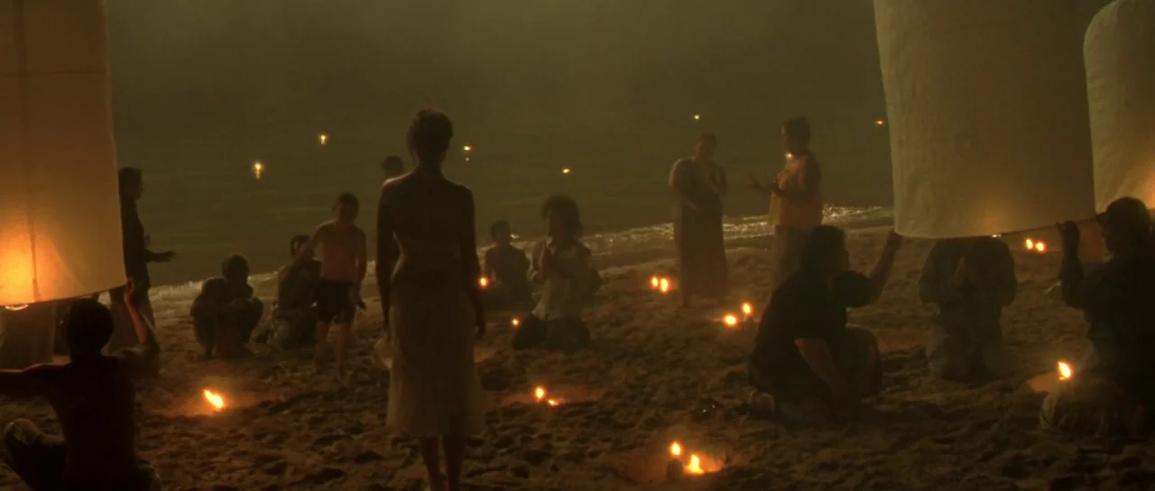 Vinyan (2008) movie still: wide — A dark, misty beach at night is illuminated by small scattered fires in the sand. A group of people gather in the…