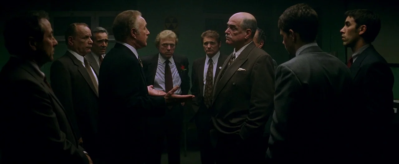 The Yards (2000) movie still: fullbody — A dimly lit industrial room contains a group of men in formal business suits. The men stand in a circle…