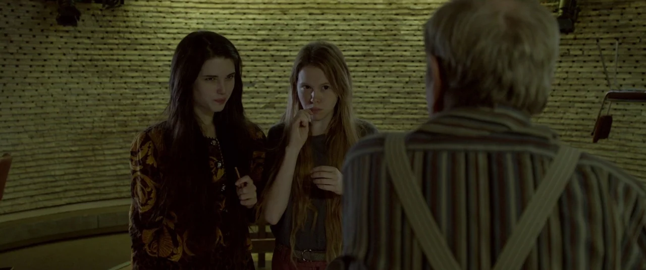 The Lure (2015) movie still: medium — An interior space with walls covered in textured wooden slats behind two young women. The two women are…