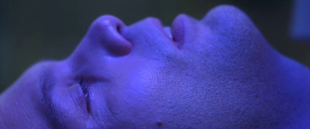 The Cell (2000) movie still: closeup — An extreme close up shows the side profile of a man's face in darkness. The subject lies still with eyes…