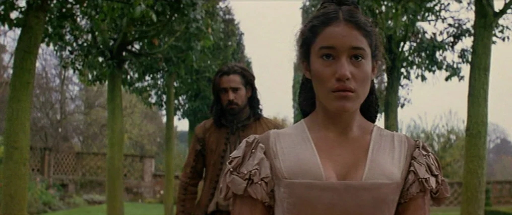 The New World (2005) movie still: medium — A tree-lined pathway runs between rows of trimmed trees in a park-like outdoor setting. A young woman in…
