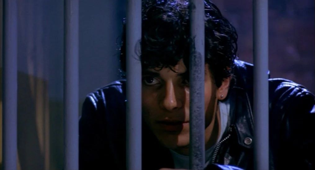 A Nightmare On Elm Street (1984) movie still: closeup — A dimly lit room is partitioned by vertical iron bars. A man gazes through the metal bars.