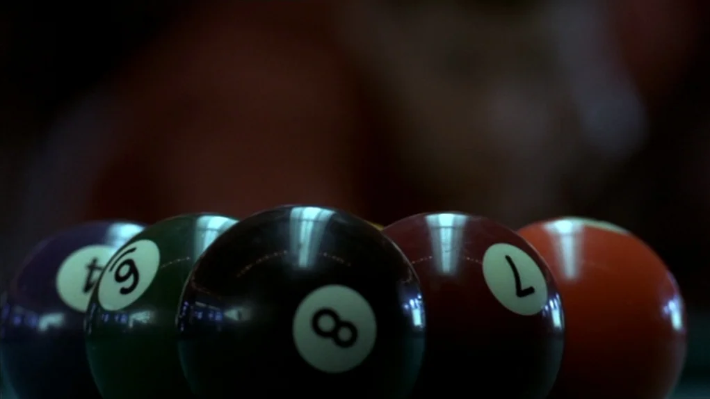 The Colour of Money (1986) movie still: closeup — A dark setting features a close-up of a cluster of colored billiards balls. The black eight ball…