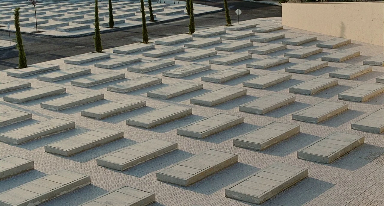 The Skin I Live In (2011) movie still: establishing — A rows of uniform concrete slabs arranged in an orderly grid across a plaza. Small trees…