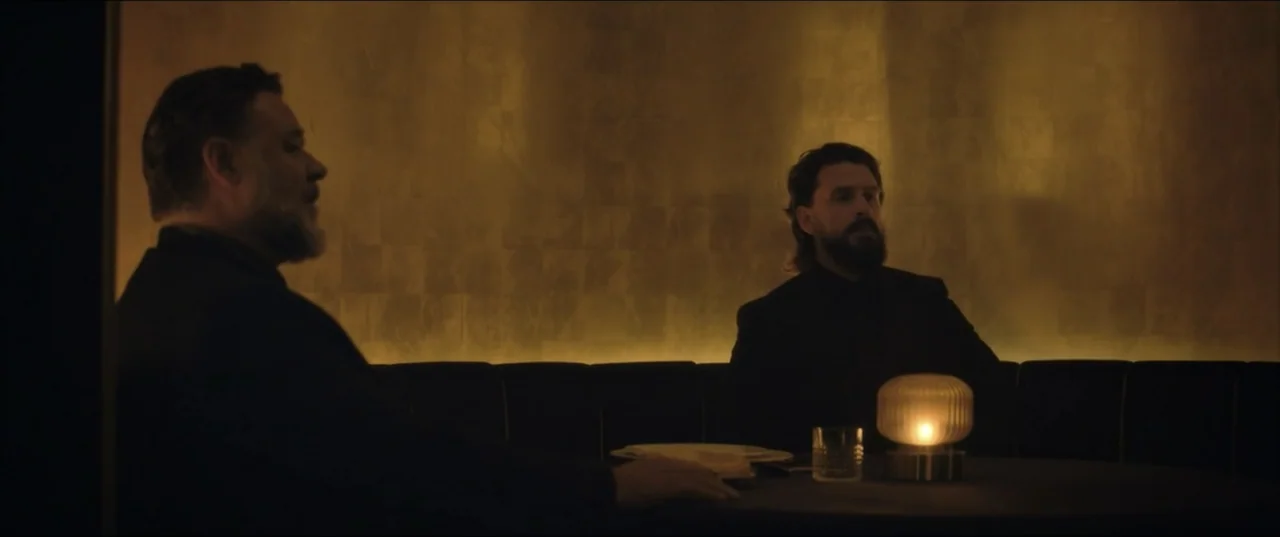 Kraven the Hunter (2024) movie still: medium — A dimly lit restaurant interior with dark paneling and a circular dining booth. Two men in dark suits…