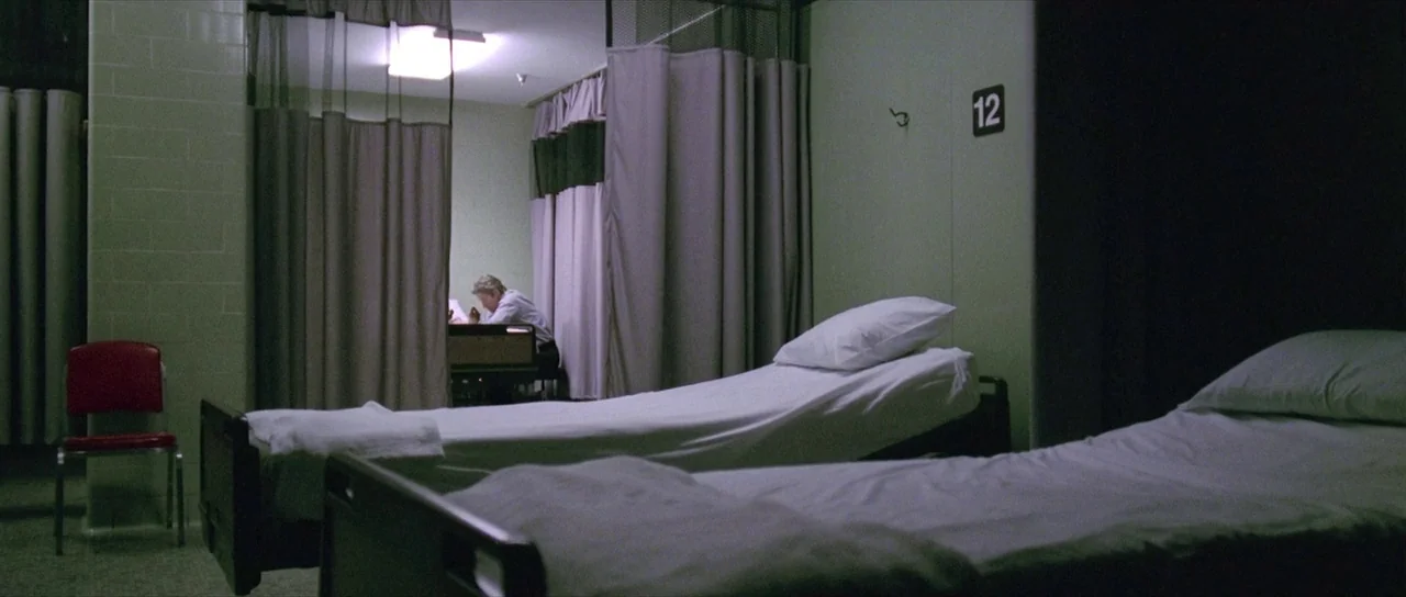 The Mothman Prophecies (2002) movie still: wide — A hospital ward features rows of beds divided by privacy curtains and pale green walls. A solitary…