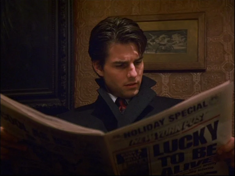 Eyes Wide Shut (1999) movie still: medium — A man sits in a dimly lit room with textured wallpaper and framed artwork. He holds an open New York…