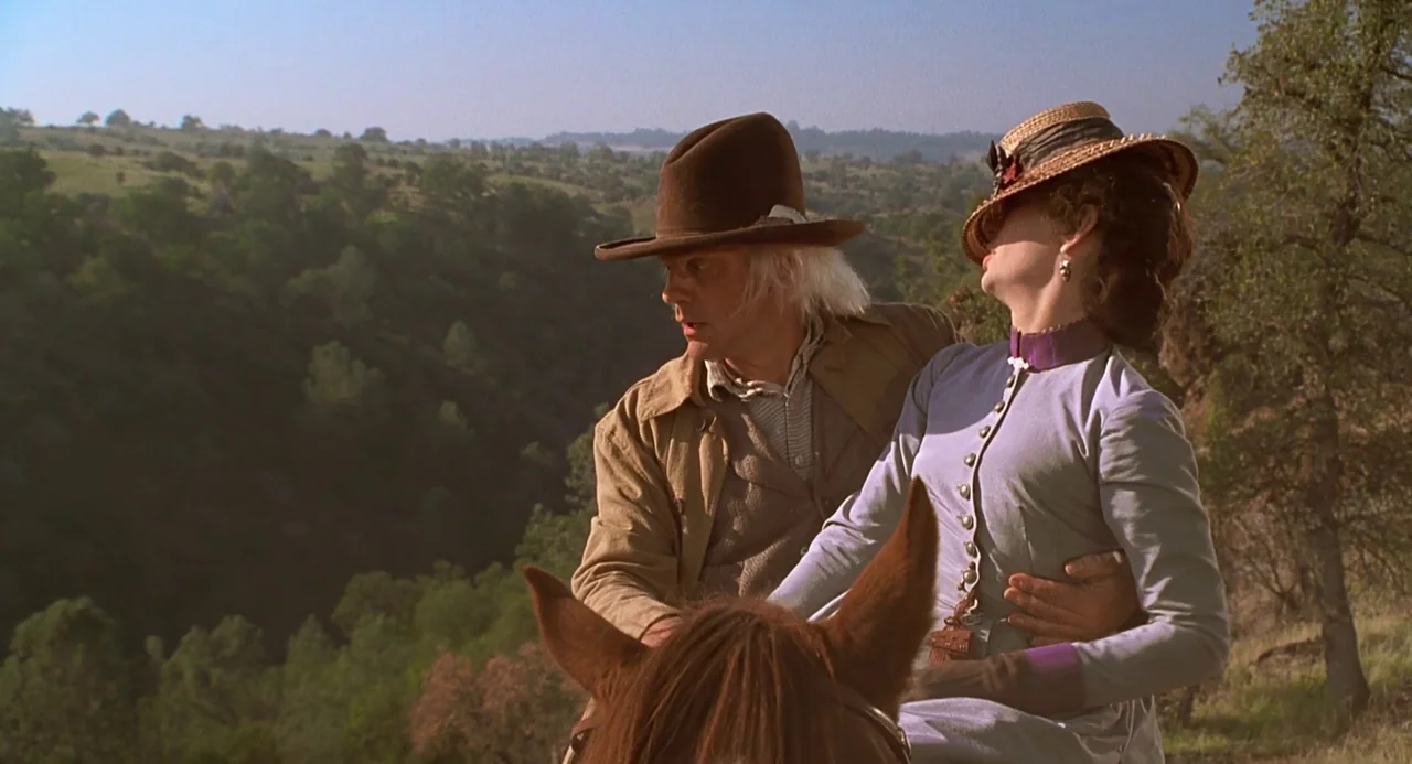 Back To The Future Part III (1990) movie still: medium — A rolling green hillside extends into a distant, hazy landscape under a clear sky. A man in…