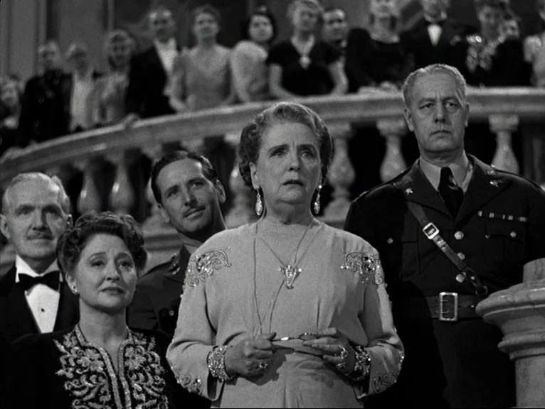Saboteur (1942) movie still: medium — A group of formally dressed people stands on a grand, ornate stone staircase. The foreground subjects are…