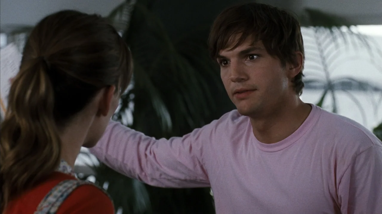 F Valentine's Day (2026) movie still: medium — A bright indoor living space features large tropical plants in the background. A man stands facing a…