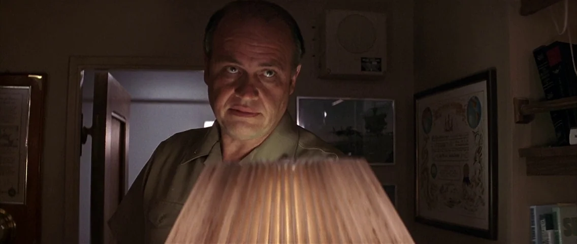 The Hunt for Red October (1990) movie still: medium — A dimly lit room with framed documents and a small light fixture visible. A man looks toward…