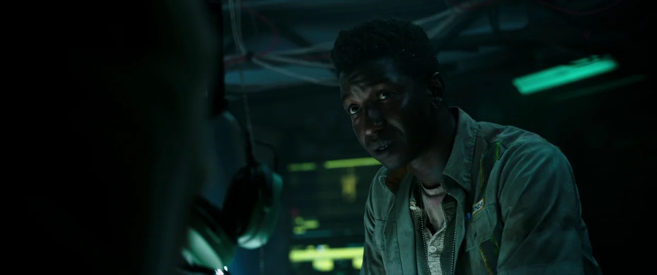 Underwater (2020) movie still: medium — A dimly lit room with tangled overhead cables and glowing green electronic display panels. A man in a work…
