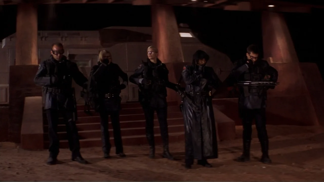 Ghosts of Mars (2001) movie still: fullbody — A night exterior site with large architectural pillars and an industrial metal structure behind. Five…