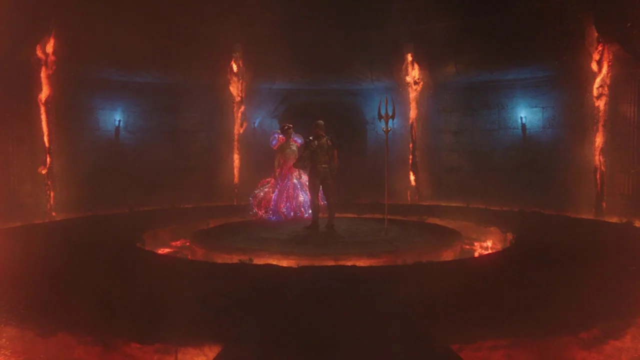 Aquaman (2018) movie still: wide — A dark subterranean circular chamber features a central raised stone platform surrounded by lava. A man stands…
