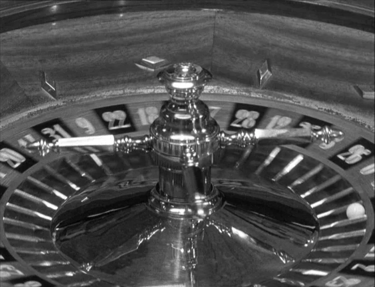 Bob le Flambeur (1956) movie still: closeup — A polished wooden and metallic roulette wheel sits on a gaming table. The white ball rests in the…