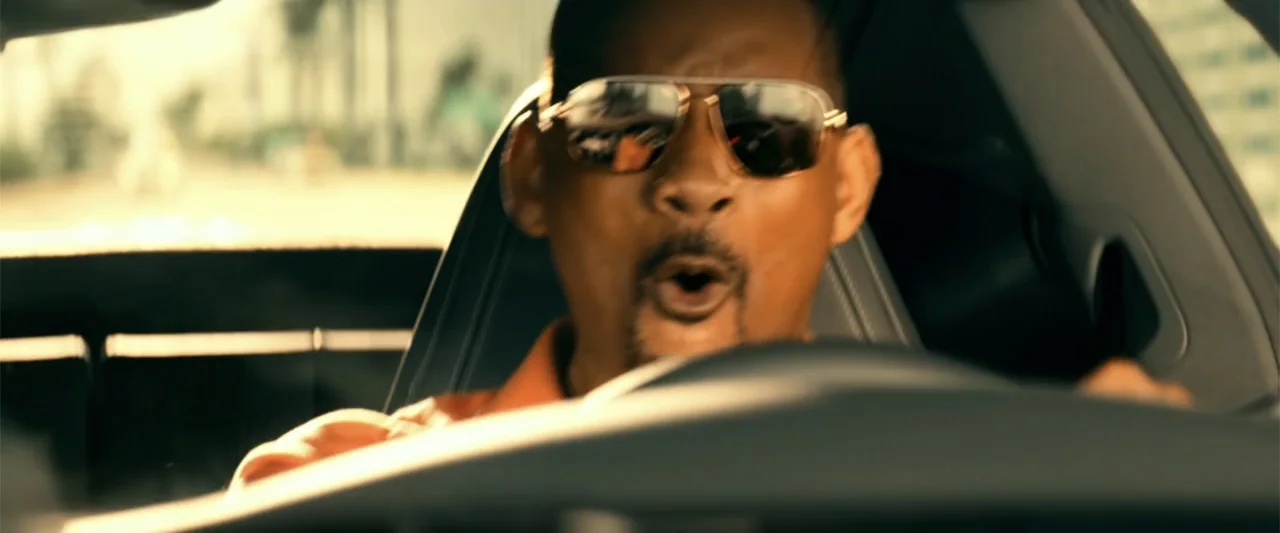Bad Boys for Life (2020) movie still: closeup — The interior of a moving car features a black steering wheel and leather headrests. A man with…