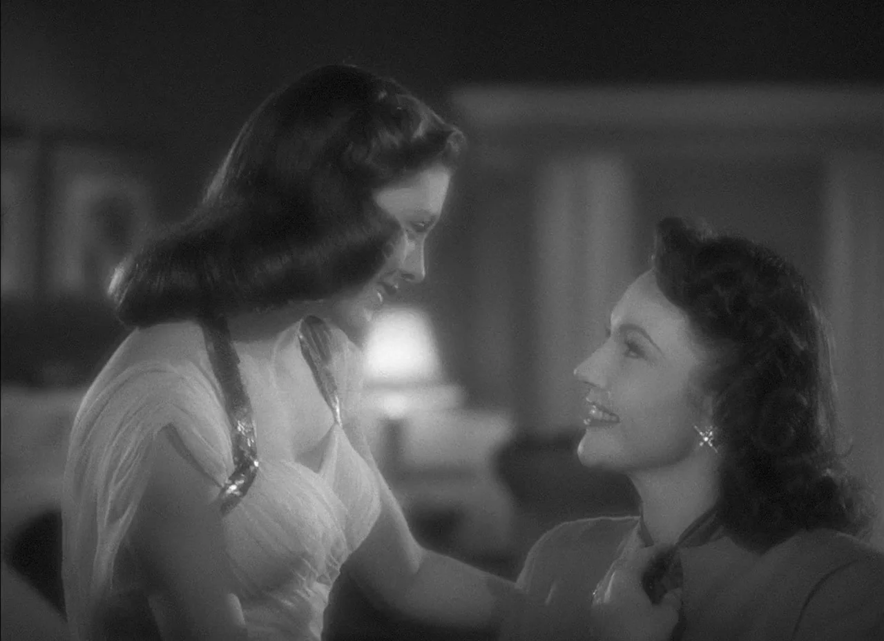 The Amazing Mr. X (1948) movie still: medium — A dimly lit room with out of focus furniture visible in the dark background. Two women stand close to…