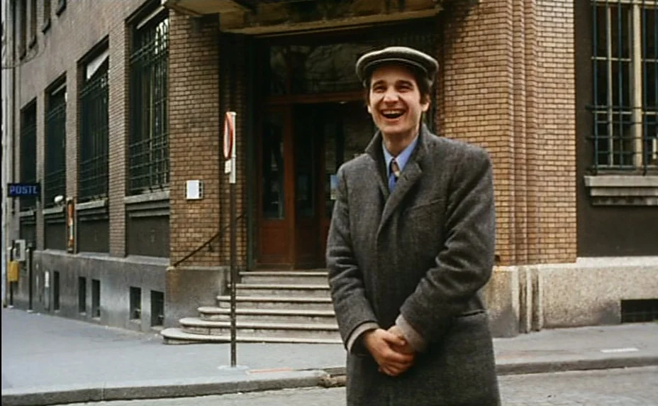 Stolen Kisses (1968) movie still: medium — A man stands on a sidewalk in front of a brick building entrance. The brick building features a set of…