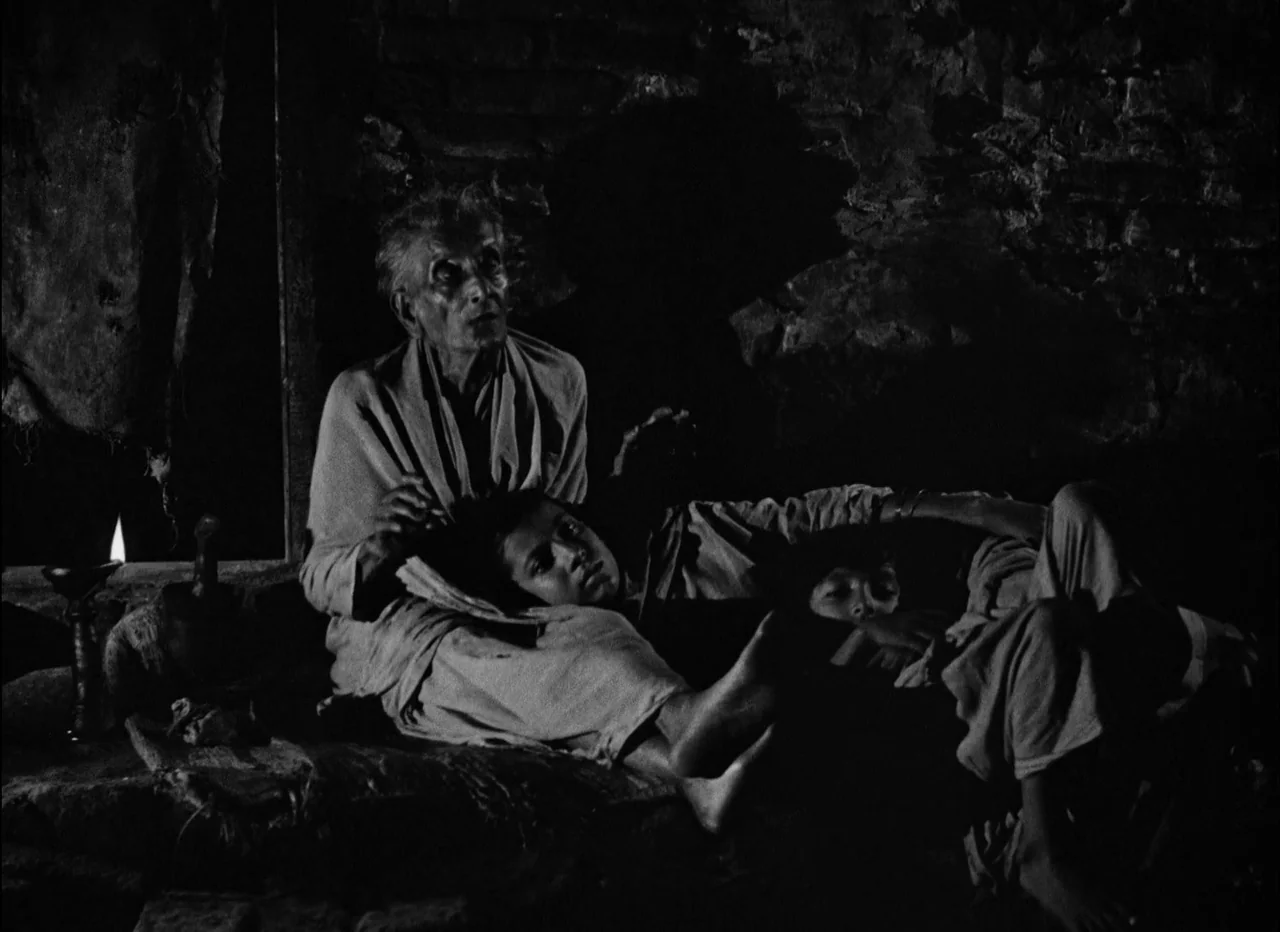 Pather Panchali (1955) movie still: medium — An interior space with rough stone walls built of earth or mud. An elderly woman sits on the floor…
