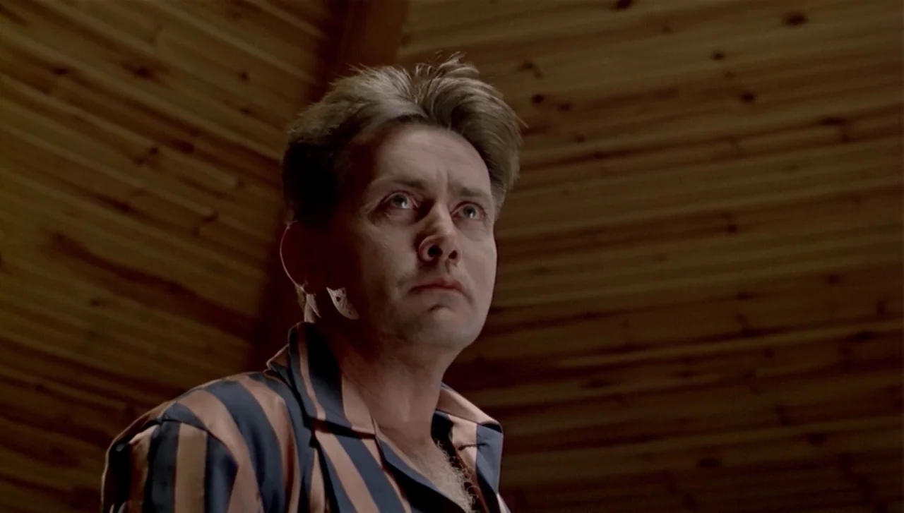 The Dead Zone (1983) movie still: closeup — A room with paneled wood ceilings and dim surroundings provides a sparse background. A man wears striped…