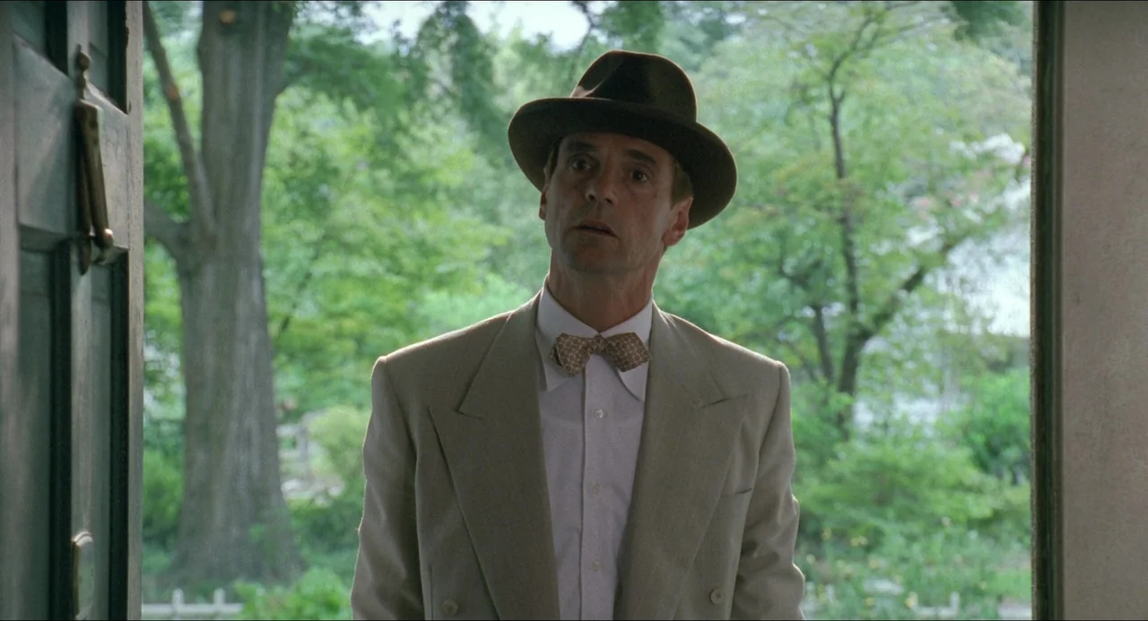 Lolita (1997) movie still: medium — A man stands in an open doorway with a lush green yard in the background. He is centered in the frame, wearing a…