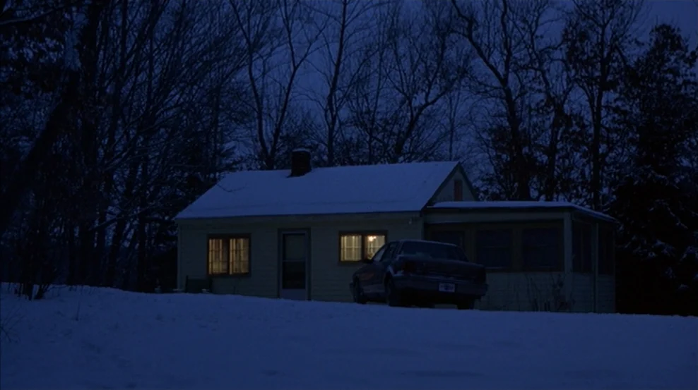 Fargo (1996) movie still: wide — A single-story house sits amidst bare trees and a snow-covered field at night. Two windows glow with warm indoor…