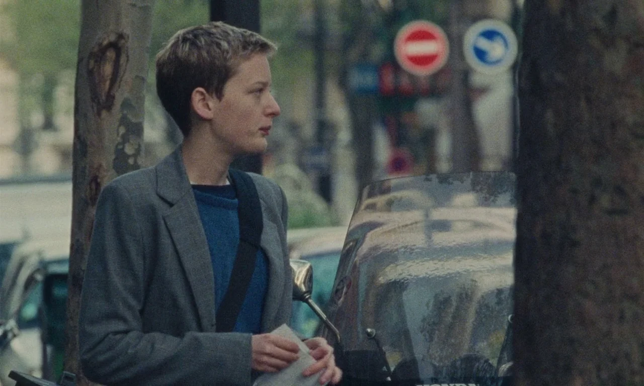 Late August, Early September (1998) movie still: medium — A city street sidewalk lined with mature trees and traffic signs in the background. A…