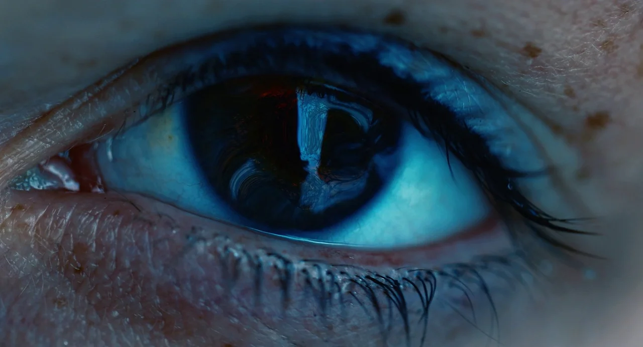 Hellbender (2021) movie still: closeup — An extreme close up of a human eye showing highly detailed iris structure. The pupil contains a reflection…