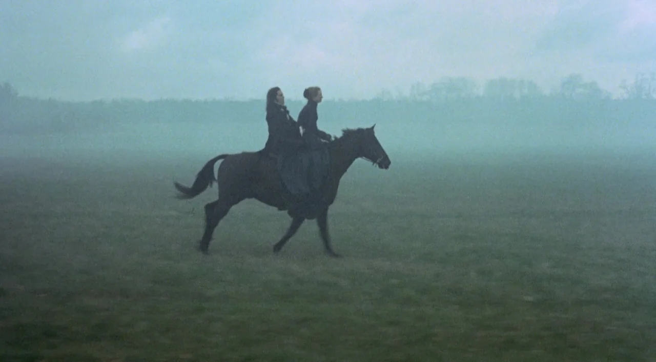 Orlando (1992) movie still: wide — A vast, open field is completely enveloped by a thick, heavy layer of grey fog. Two people sit side-by-side on a…