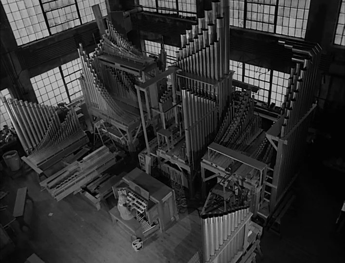 Carnival of Souls (1962) movie still: wide — A spacious workshop contains a large, multi-section pipe organ undergoing assembly or maintenance. A…