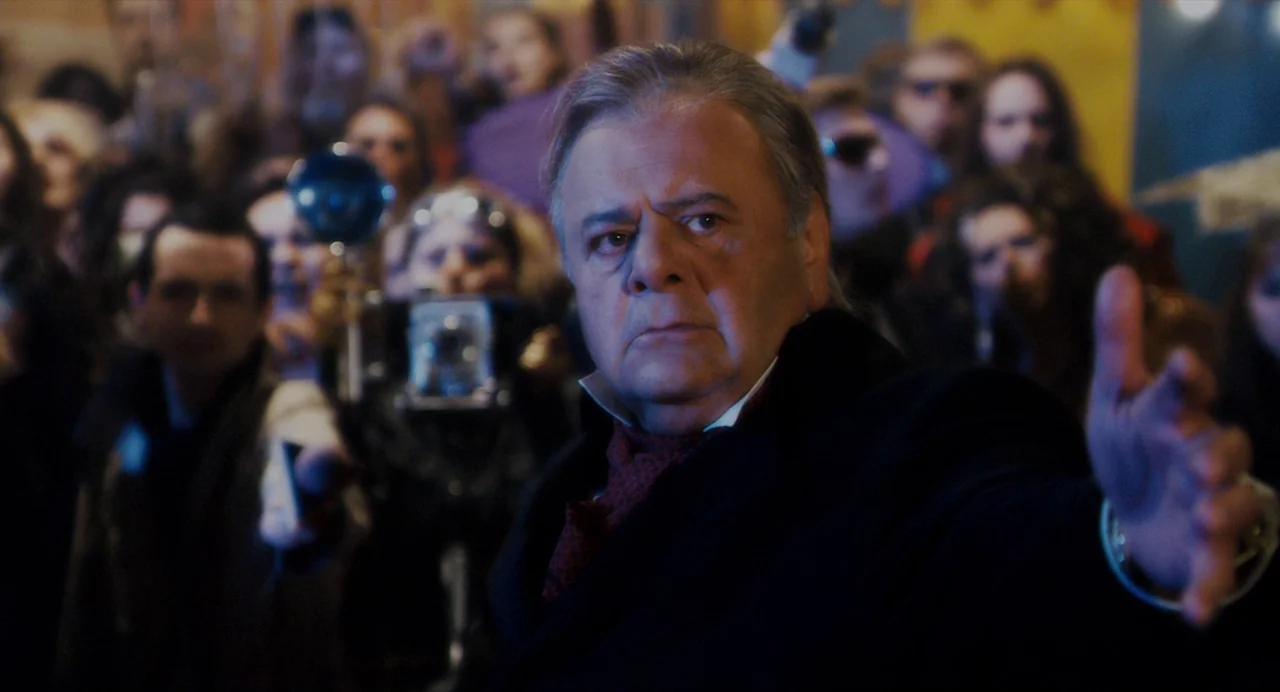 Repo! The Genetic Opera (2008) movie still: medium — A middle-aged man stands in a dense, dimly lit crowd of onlookers at night. He reaches out a…