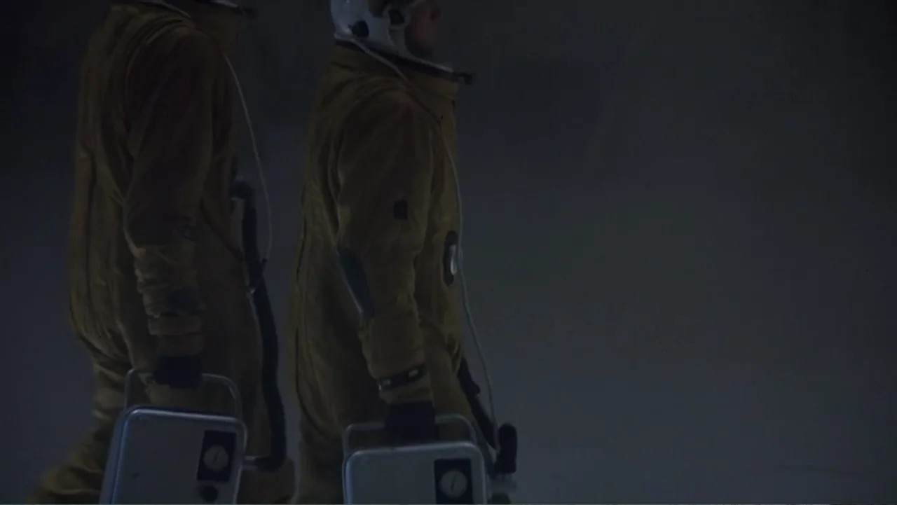 Crisis Point (2012) movie still: medium — Two individuals in yellow space suits move across a dark, featureless expanse at night. They hold metal…