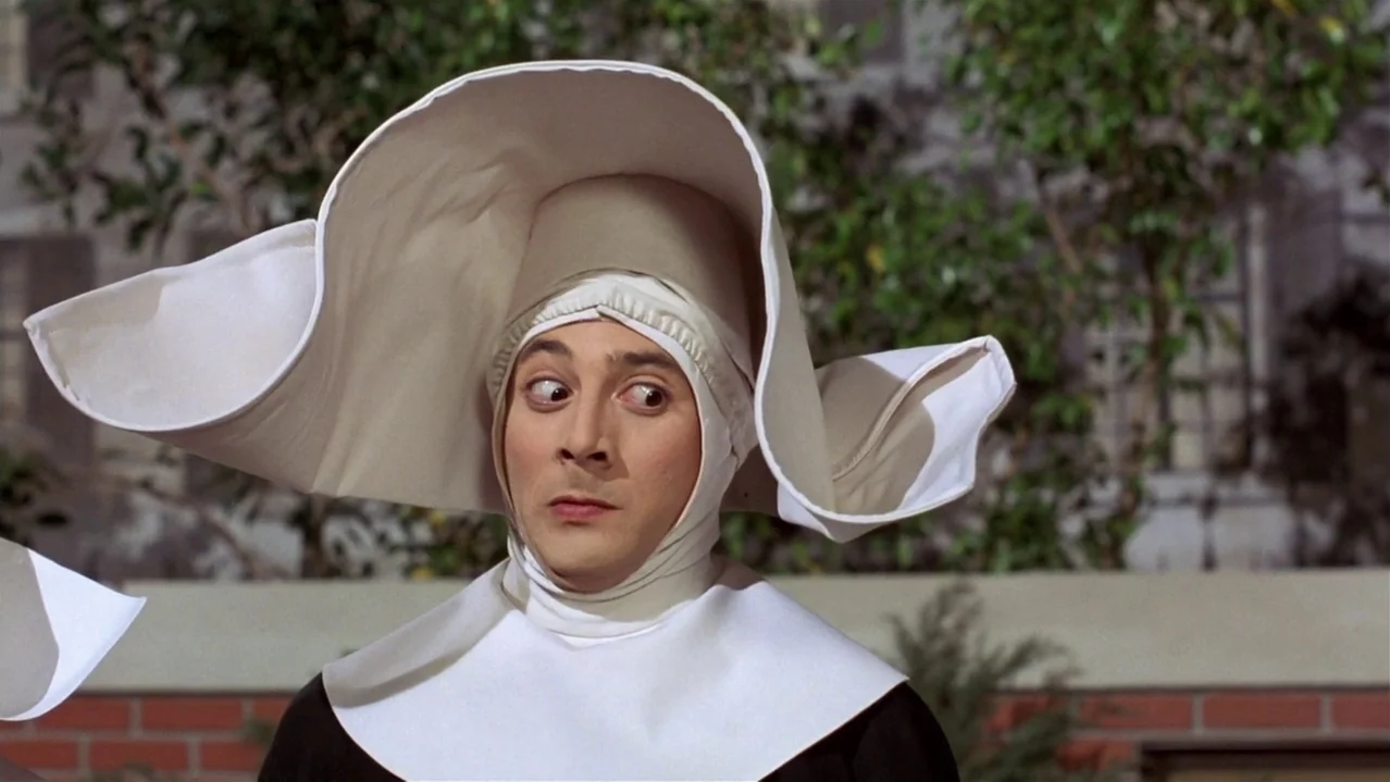 Pee-Wee’s Big Adventure (1985) movie still: closeup — A person wears a large white starched wimple in an outdoor setting. The subject glances to the…