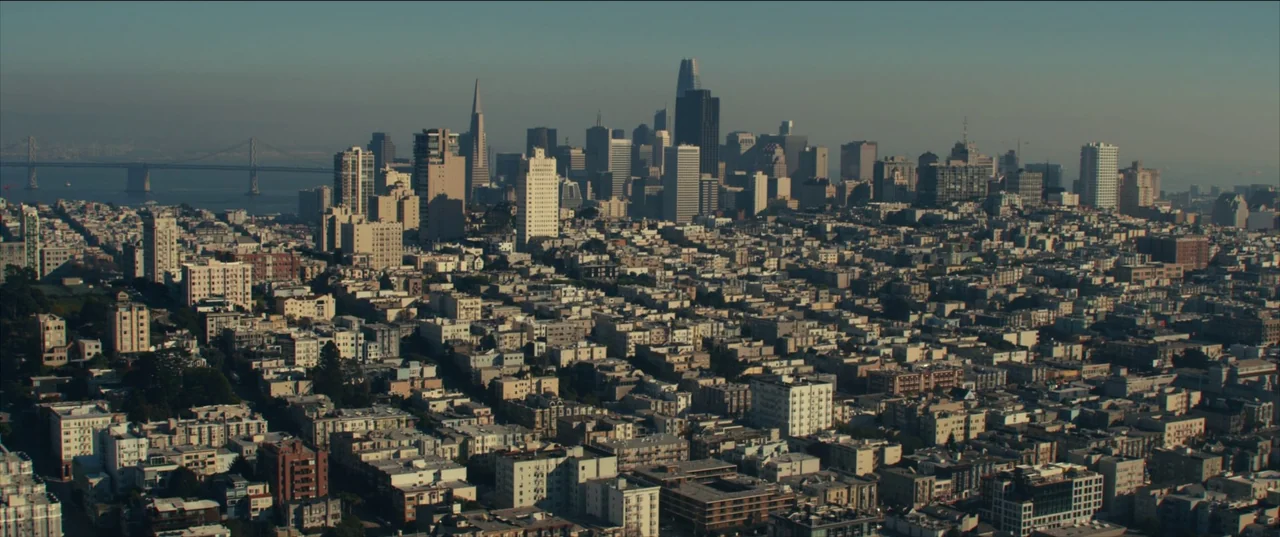 The Invisible Man (2020) (2020) movie still: establishing — A dense urban sprawl stretches toward a distant modern skyline and a large bridge.…