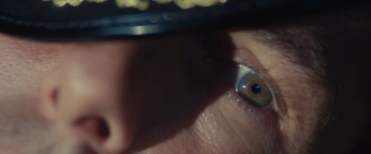 Edge of Tomorrow (2014) movie still: closeup — An extreme close-up of a man's eye viewed from beneath a dark hat brim. The iris catches a sliver of…