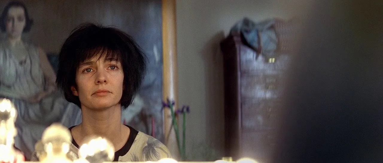 Nikita (1990) movie still: medium — A woman sits before a vanity mirror lit by a row of bright bulbs. A large painting of a figure hangs on the wall…
