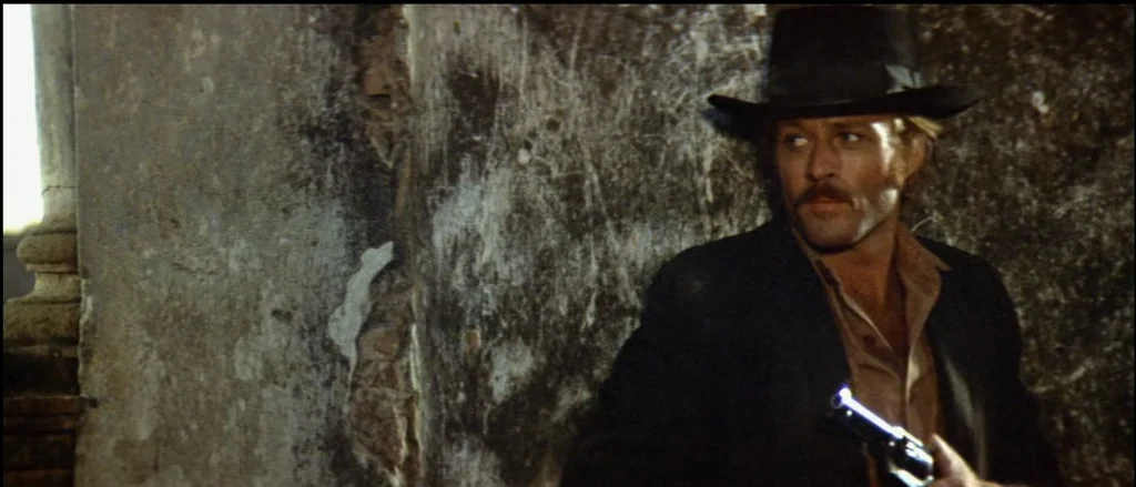 Butch Cassidy and the Sundance Kid (1969) movie still: medium — A man stands beside a crumbling stone pillar with heavy weathering and deep cracks.…