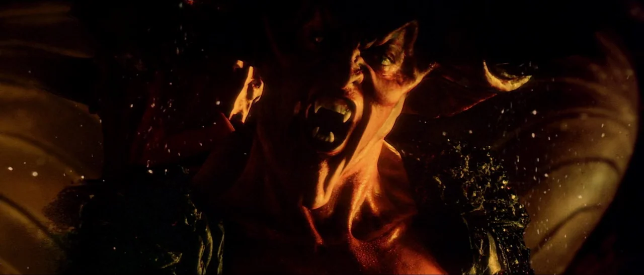 Legend (1985) movie still: closeup — A demonic creature with large horns stands in a dark, warm-lit environment. The subject roars with bared fangs…