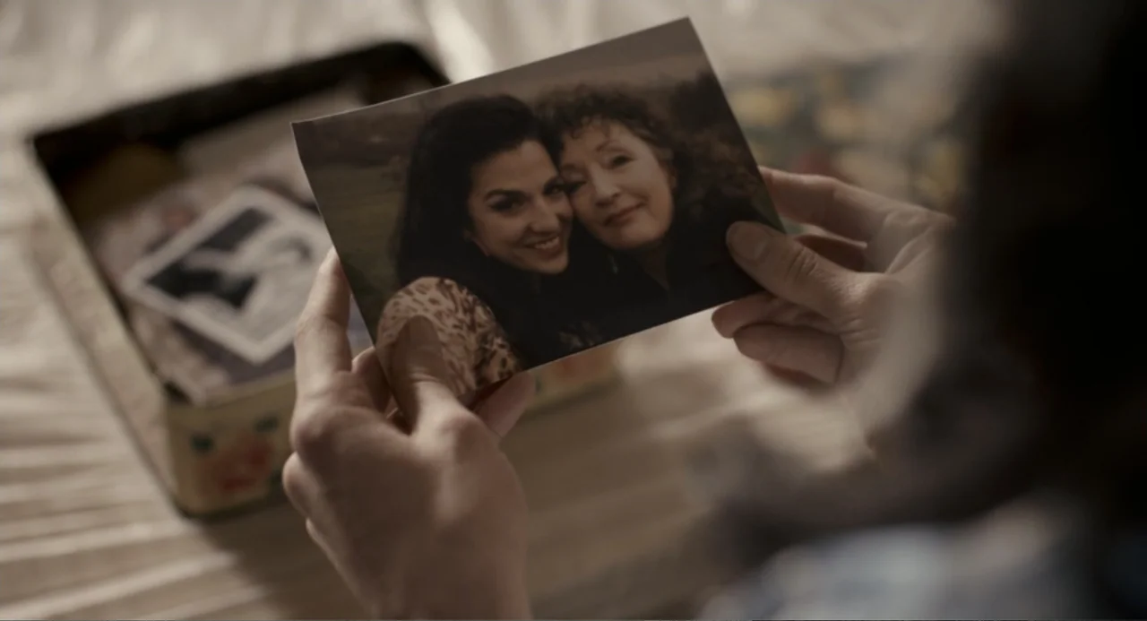 Back to Black (2024) movie still: closeup — A person holds a physical photograph featuring two women while sitting indoors. The photograph shows a…