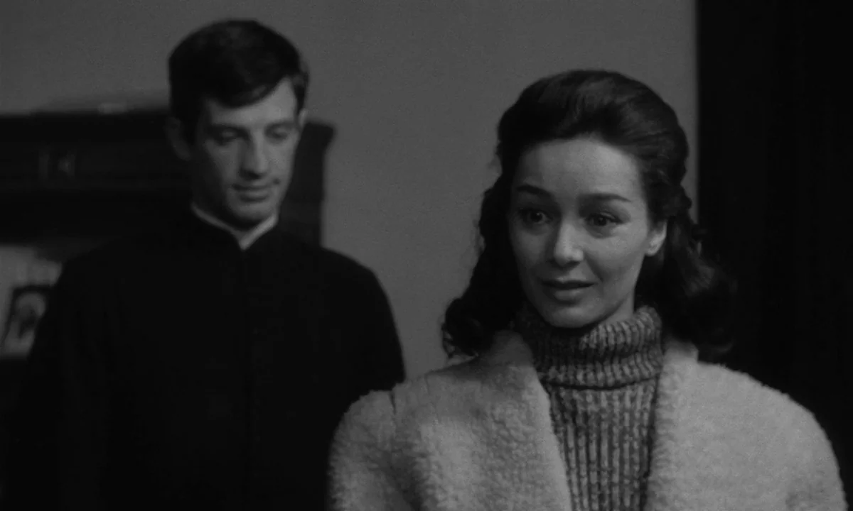 Léon Morin, Priest (1961) movie still: medium — A dimly lit domestic interior with a woman in the foreground and a man blurred. The woman looks…
