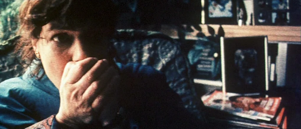 Wonderland (1999) movie still: closeup — A cluttered work space filled with framed photographs and stacks of magazines on shelves. A woman sits in…