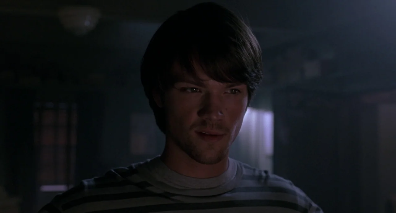 House of Wax (2005) movie still: closeup — A dark, dimly lit indoor space with obscured background details. A young man stares directly ahead in the…