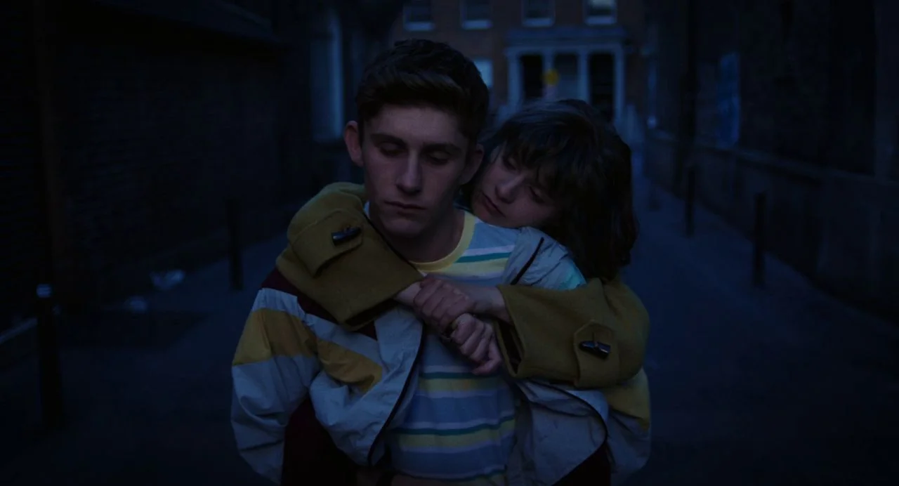 Dating Amber movie still: medium — A dimly lit narrow urban passageway stretches into the dark background at night. A young woman gives a teenage…