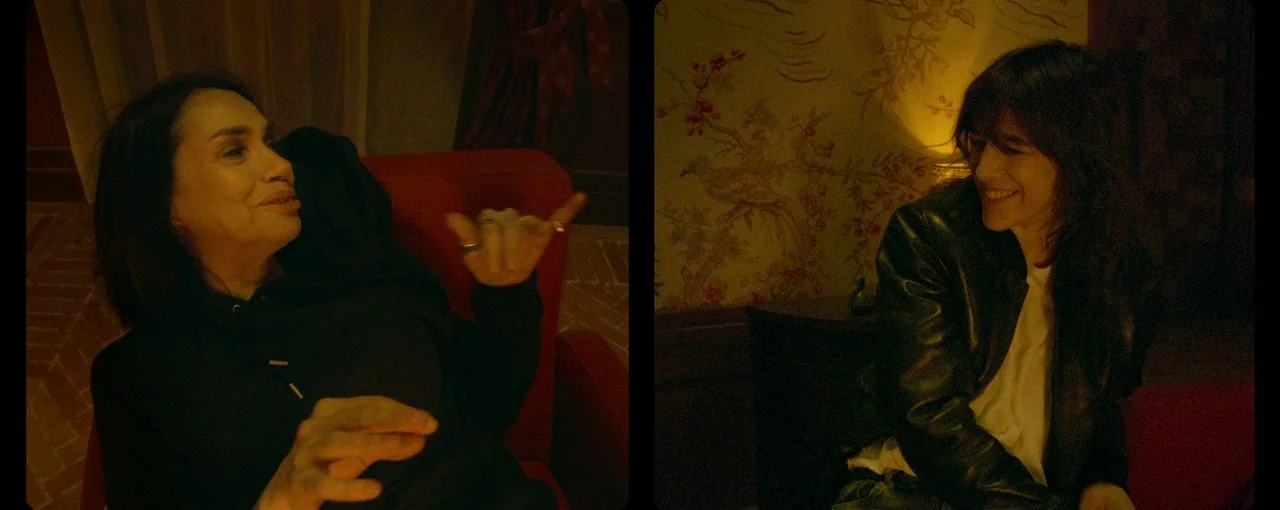 Lux Æterna (2019) movie still: medium — A split-screen composition shows two people conversing in a dimly lit, warm-toned interior. Each subject…